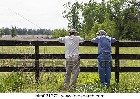 Stock Image - Caucasian father and son leaning on fence by rural field. Fotosearch