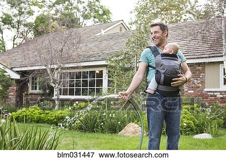 Stock Photo - Caucasian father holding baby and watering plants. Fotosearch