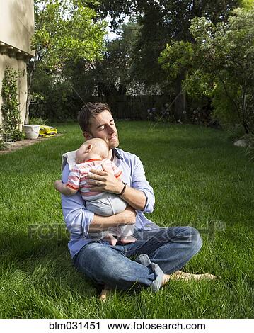 Stock Image - Caucasian father holding baby in backyard. Fotosearch