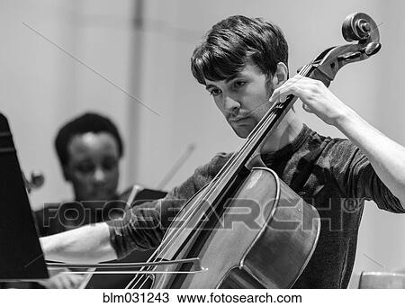 Stock Image - Caucasian student playing cello in college orchestra. Fotosearch