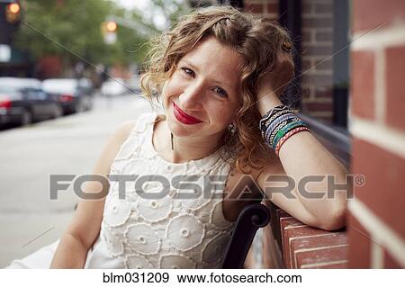 Stock Photo - Caucasian woman sitting on bench on city street. Fotosearch