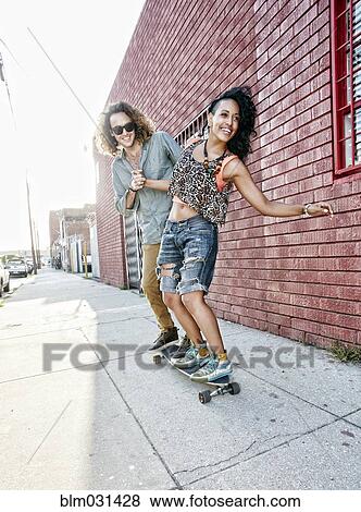 Stock Photo - Couple riding skateboard on city street. Fotosearch