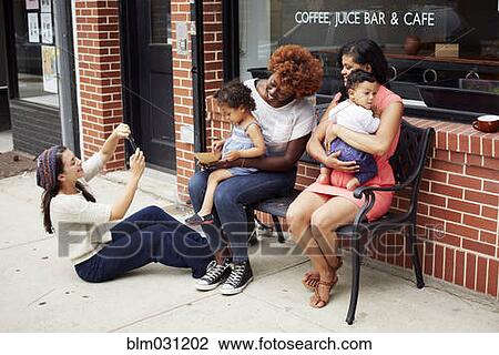 Stock Image - Friends taking cell phone pictures together on city street. Fotosearch