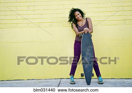 Hispanic woman holding skateboard on city street View Large Photo Image Stock Image - Hispanic woman holding skateboard on city street. Fotosearch