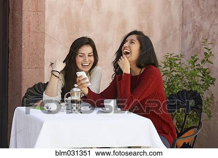 Stock Image - Hispanic women using cell phone at sidewalk cafe. Fotosearch