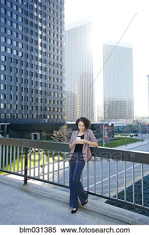 Stock Photography - Mixed race businesswoman using cell phone on urban sky bridge. Fotosearch
