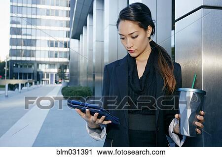 Stock Image - Mixed race businesswoman using tablet computer on city street. Fotosearch