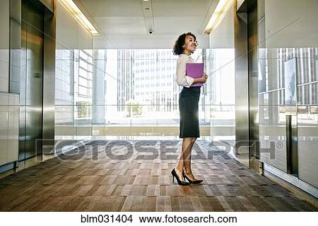 Picture - Mixed race businesswoman waiting for elevator in lobby. Fotosearch