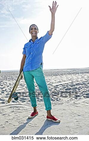 Stock Photography - Older Black woman holding skateboard on beach. Fotosearch