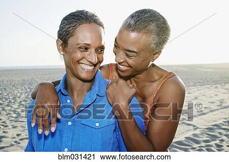 Stock Image - Older Black women hugging on beach. Fotosearch