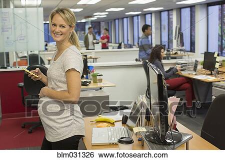 Stock Photograph - Pregnant businesswoman using cell phone in office. Fotosearch