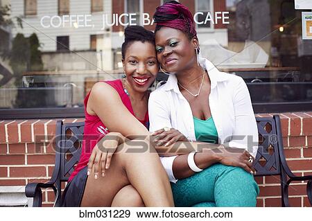Stock Photo - Woman sitting together outside coffee shop on city street. Fotosearch