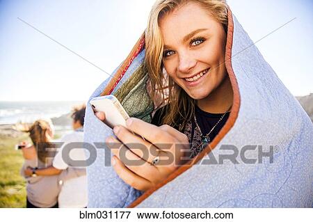 Stock Photo - Woman using cell phone in blanket on rural hillside. Fotosearch