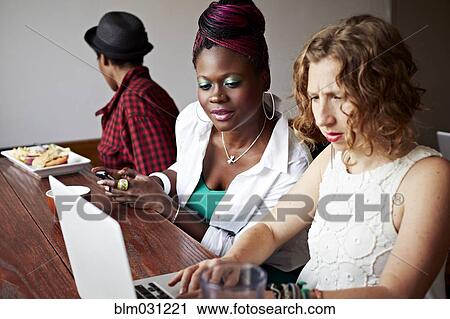 Stock Image - Women using laptop together in cafe. Fotosearch