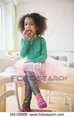 Stock Photo - African American girl eating apple at kitchen table. Fotosearch