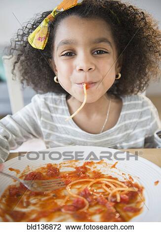 Stock Image - African American girl eating spaghetti at table. Fotosearch