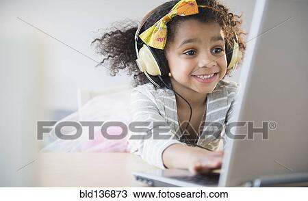 Stock Image - African American girl listening to headphones and using laptop. Fotosearch