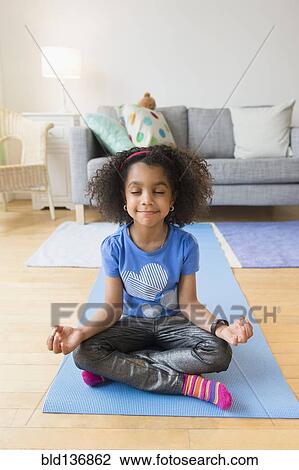 Stock Image - African American girl meditating on yoga mat. Fotosearch