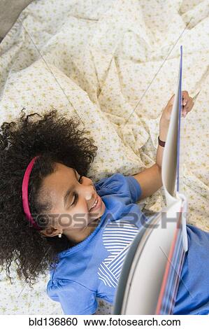 Stock Image - African American girl reading on blanket. Fotosearch