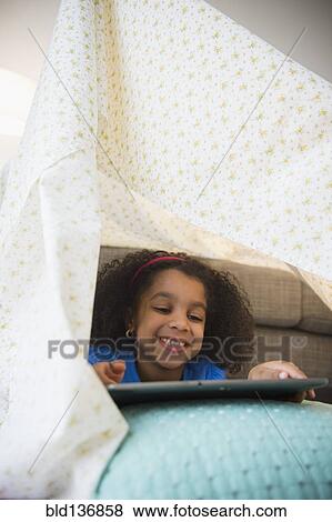 Stock Photo - African American girl using tablet computer in blanket fort. Fotosearch