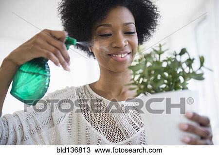 Stock Image - African American woman watering plants. Fotosearch