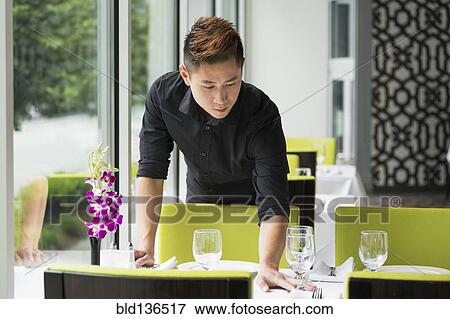 Stock Photo - Asian waiter setting table in restaurant. Fotosearch