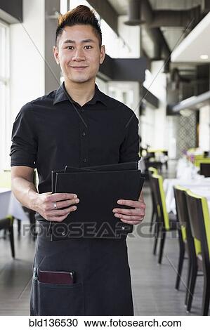 Stock Image - Asian waiter standing in restaurant. Fotosearch