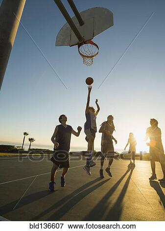 Stock Photo - Back lit basketball teams playing on court. Fotosearch