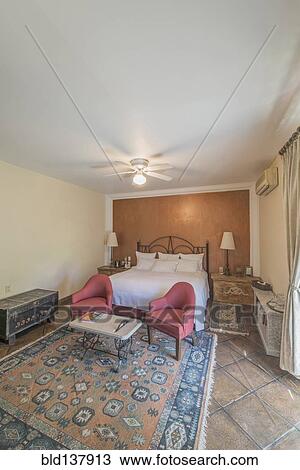 Stock Image - Bed, chairs and trunks in traditional hotel room. Fotosearch