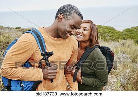 Stock Image - Black couple hiking on rural hillside. Fotosearch