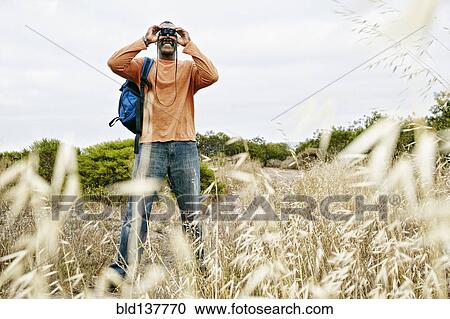 Stock Image - Black man hiking on rural hillside. Fotosearch