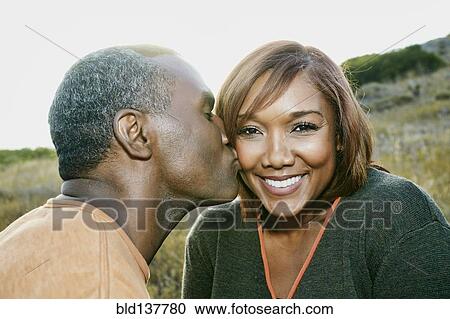 Stock Image - Black man kissing girlfriend on rural hillside. Fotosearch
