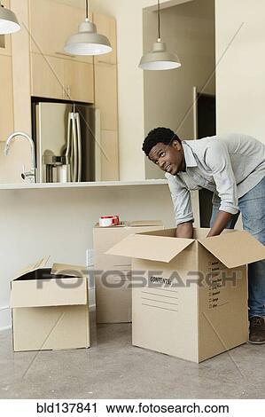 Stock Image - Black man unpacking cardboard box in new house. Fotosearch