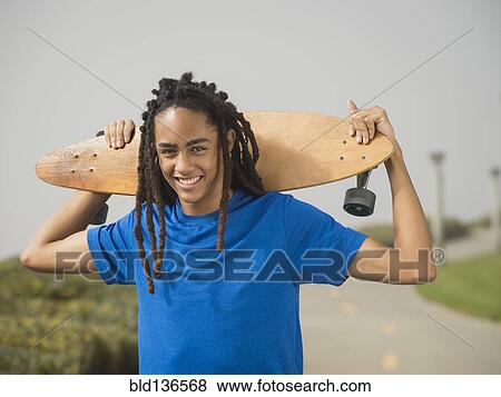 Stock Photo - Black teenage boy carrying skateboard on street. Fotosearch