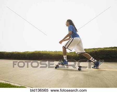 Stock Photography - Black teenage boy riding skateboard on street. Fotosearch