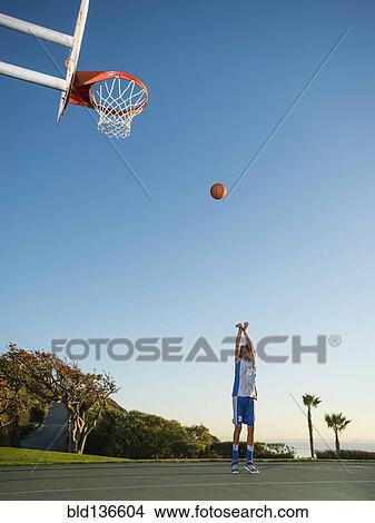 Picture - Black teenage boy shooting basketball on court. Fotosearch