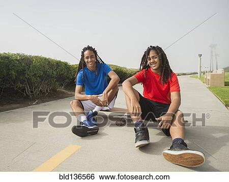 Stock Photograph - Black teenage boys sitting on skateboards on street. Fotosearch