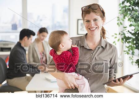 Picture - Businesswoman holding baby in office. Fotosearch