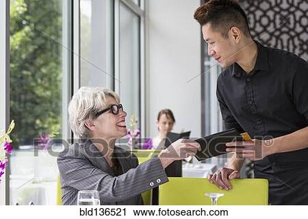 Stock Image - Businesswoman paying tab in restaurant. Fotosearch