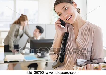 Stock Image - Businesswoman talking on cell phone in office. Fotosearch