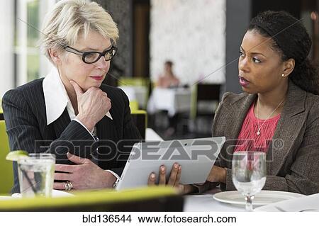 Picture - Businesswomen using tablet computer in restaurant. Fotosearch