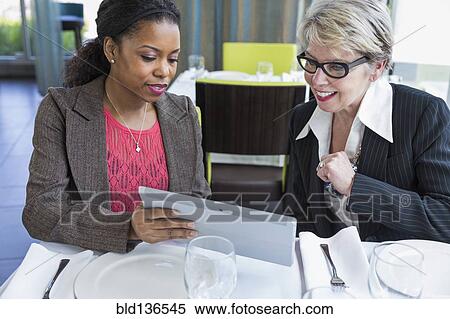 Stock Photography - Businesswomen using tablet computer in restaurant. Fotosearch