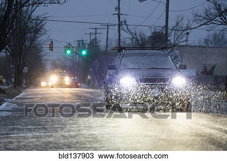 Stock Image - Car driving on snowy urban street at night. Fotosearch