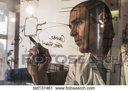 Stock Image - Caucasian businessman writing on glass. Fotosearch