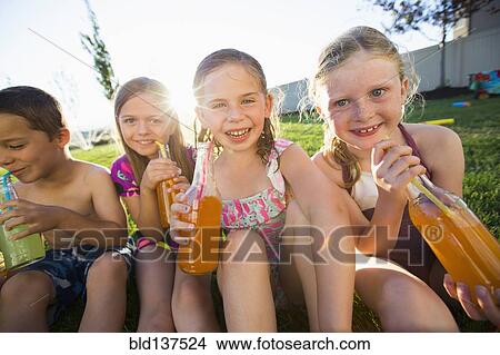 Picture - Caucasian children drinking soda in backyard. Fotosearch