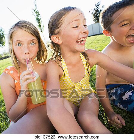 Stock Image - Caucasian children drinking soda in backyard. Fotosearch