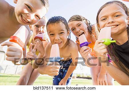 Stock Image - Caucasian children eating popsicles outdoors. Fotosearch