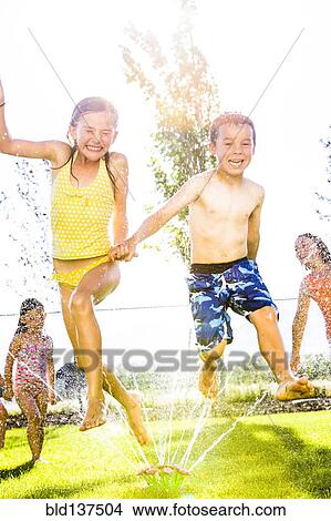 Picture - Caucasian children playing in sprinkler in backyard. Fotosearch