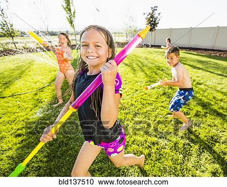 Stock Image - Caucasian children playing in sprinkler in backyard. Fotosearch