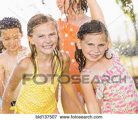 Stock Photo - Caucasian children playing in sprinkler in backyard. Fotosearch